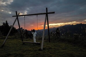 A person standing on a swing set in a grassy field with a sunset in the background. - BZIKA Wonderland Retreat (Zhangjiajie)