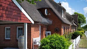 A red brick building with a thatched roof, a white picket fence, and a bench outside. - Holiday Home 'Ferienhaus Pellworm Findling' with Terrace,  Garden and Wi-Fi (Pellworm)