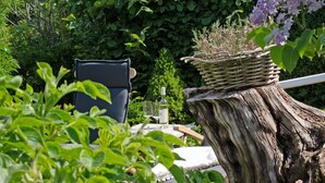 A garden setting with a wicker basket on a tree stump, a chair, and a table with a bottle and glass. - Holiday Home 'Ferienhaus Pellworm Findling' with Terrace,  Garden and Wi-Fi (Pellworm)