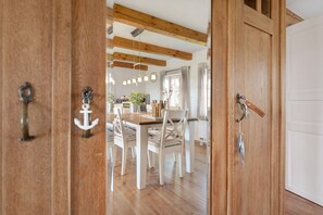 A wooden door with an anchor handle, leading to a dining area with a wooden table and white chairs. - Holiday Home 'Ferienhaus Pellworm Findling' with Terrace,  Garden and Wi-Fi (Pellworm)