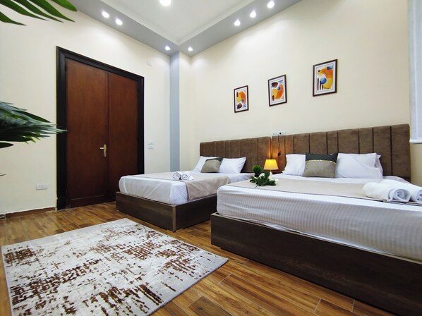 A hotel room with two beds, a wooden floor, a large rug, and three wall-mounted artworks. - Royal Central Home in Cairo (Cairo)