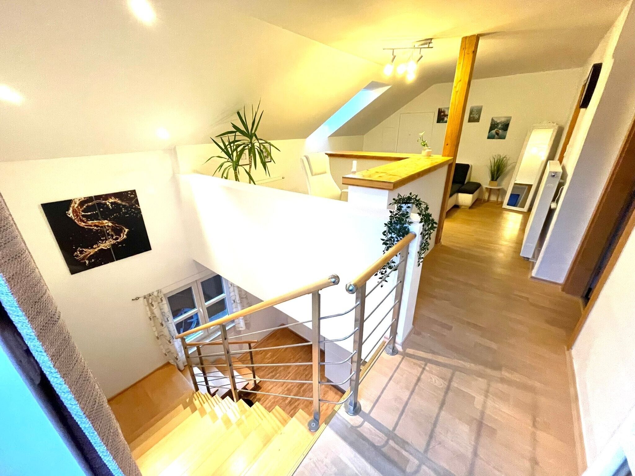A staircase leading to a loft area with a wooden floor, a white railing, and a plant on the landing.