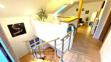A staircase leading to a loft area with a wooden floor, a white railing, and a plant on the landing.