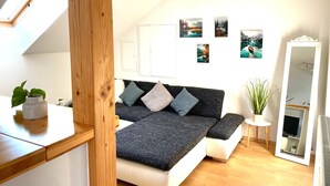 Ein modernes Schlafzimmer mit einem Schlafplatz im Loft-Stil, einem kleinen Nachttischchen mit Pflanze, einem Spiegel und Wandbildern.