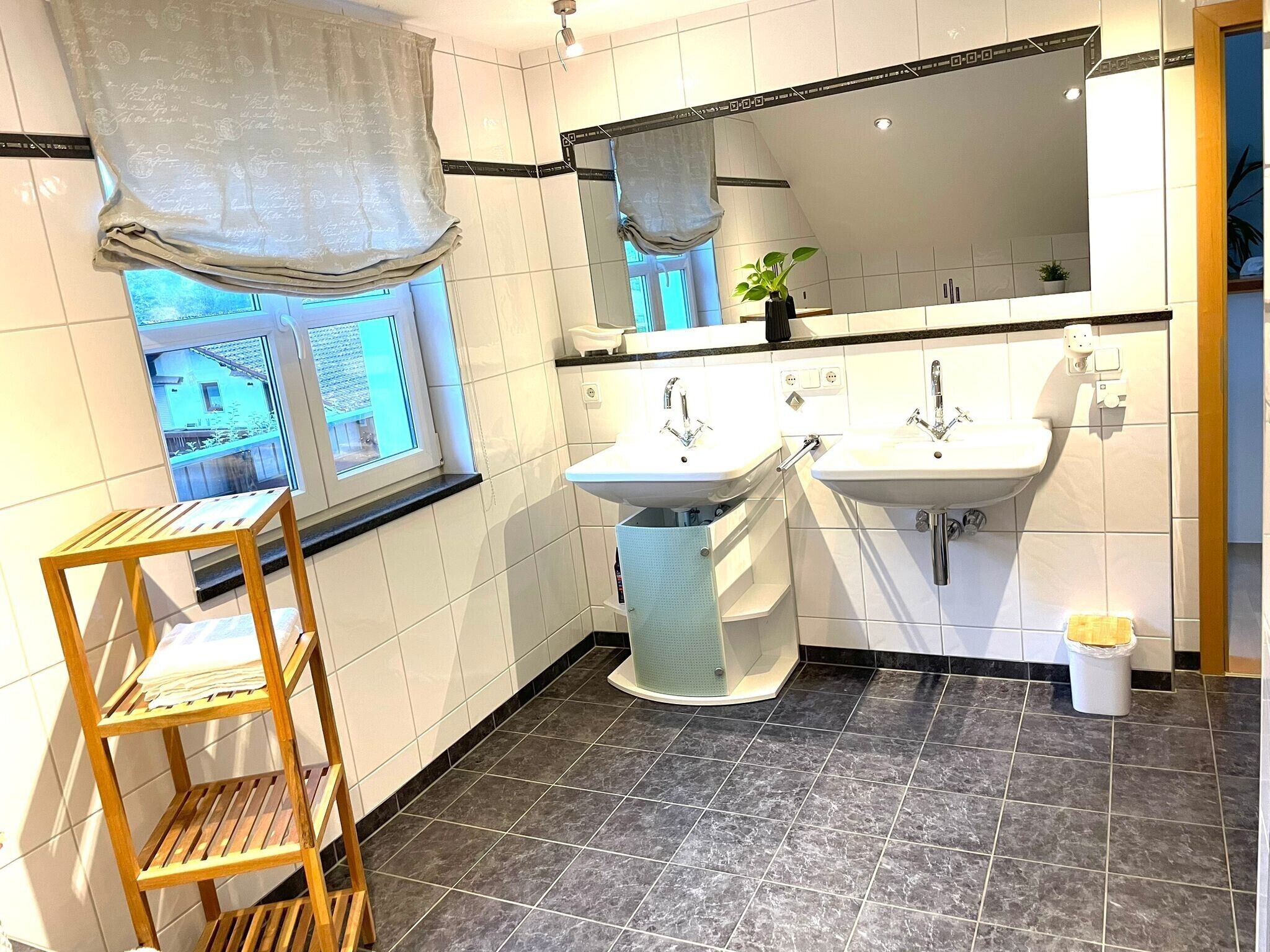 A bathroom with two sinks, a window with a view, a wooden shelf, and a mirror.