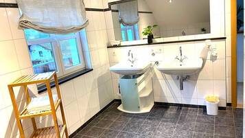 A bathroom with two sinks, a window with a view, a wooden shelf, and a mirror.