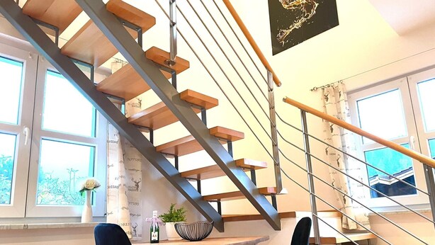 Ein modernes Interieur mit einer Holztreppe, einem Essbereich mit zwei Stühlen und einem Tisch mit Flasche und Schale.