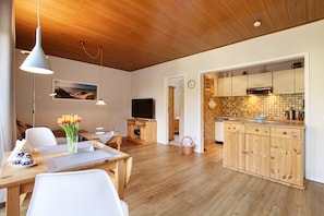 Une cuisine moderne avec des meubles en bois et un pare-feu en carreaux, un coin repas avec une table et des chaises, et un salon avec un téléviseur et des œuvres d’art accrochées au mur.
