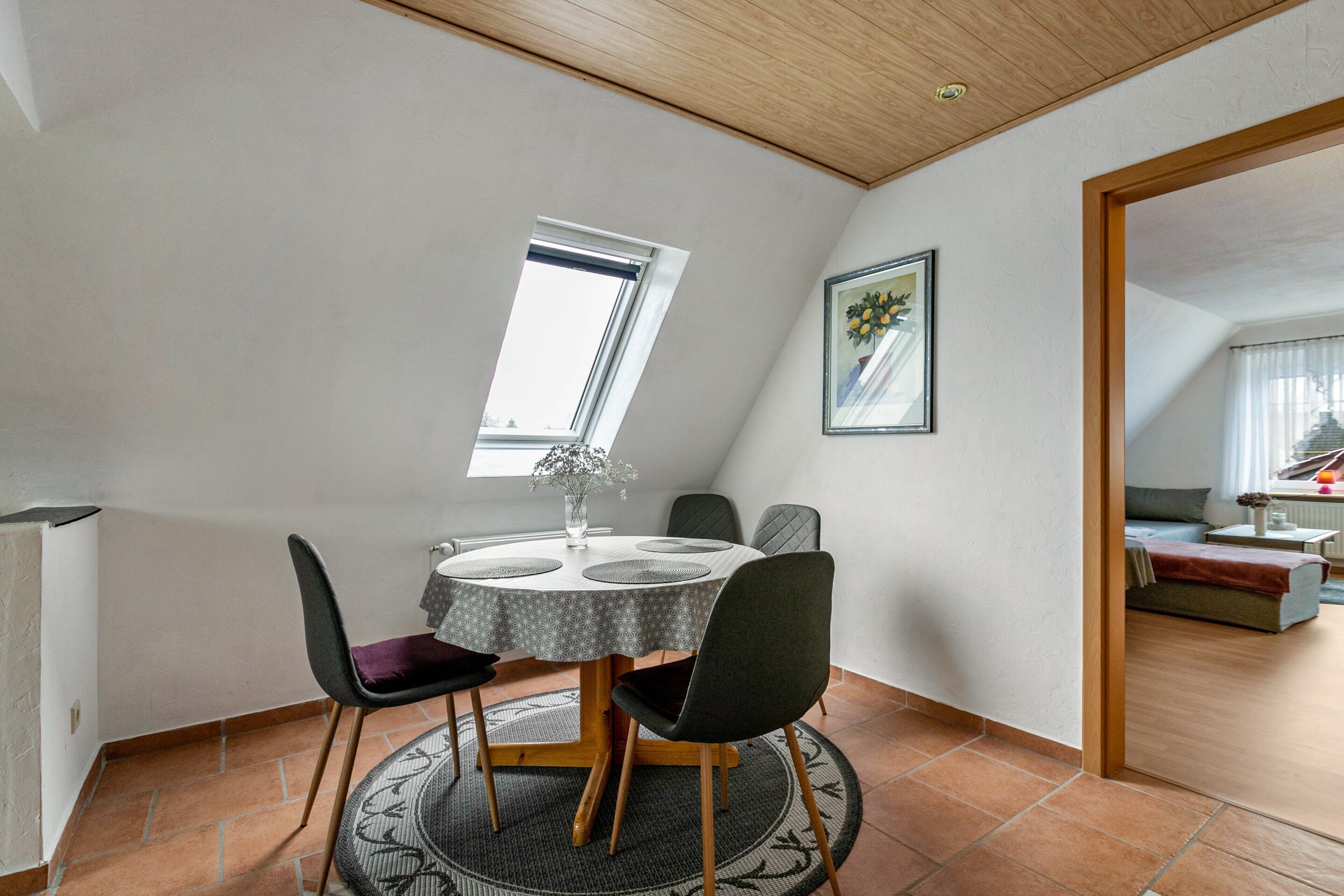 A dining area with a round table, chairs, a window, and a painting on the wall.
