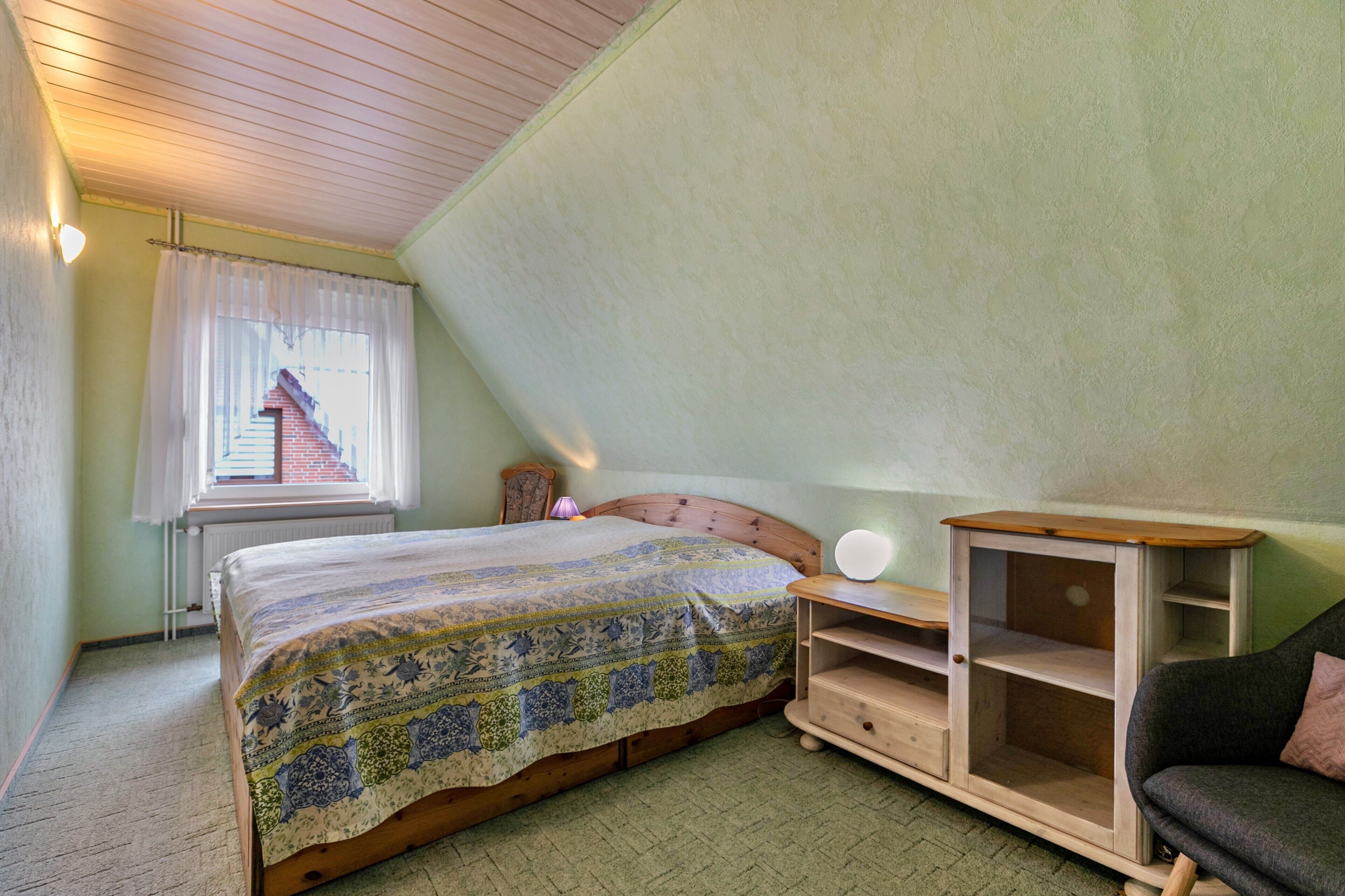 A bedroom with a bed, a nightstand, a dresser, and a window with curtains.