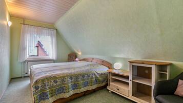 A bedroom with a bed, a nightstand, a dresser, and a window with curtains.