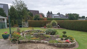 Un jardin aménagé avec une variété de plantes et de fleurs, un petit étang et un banc en métal.
