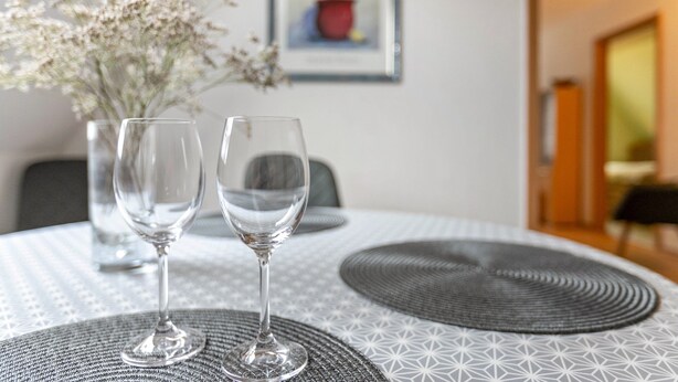 Une table à manger avec deux verres à vin et un vase de fleurs.