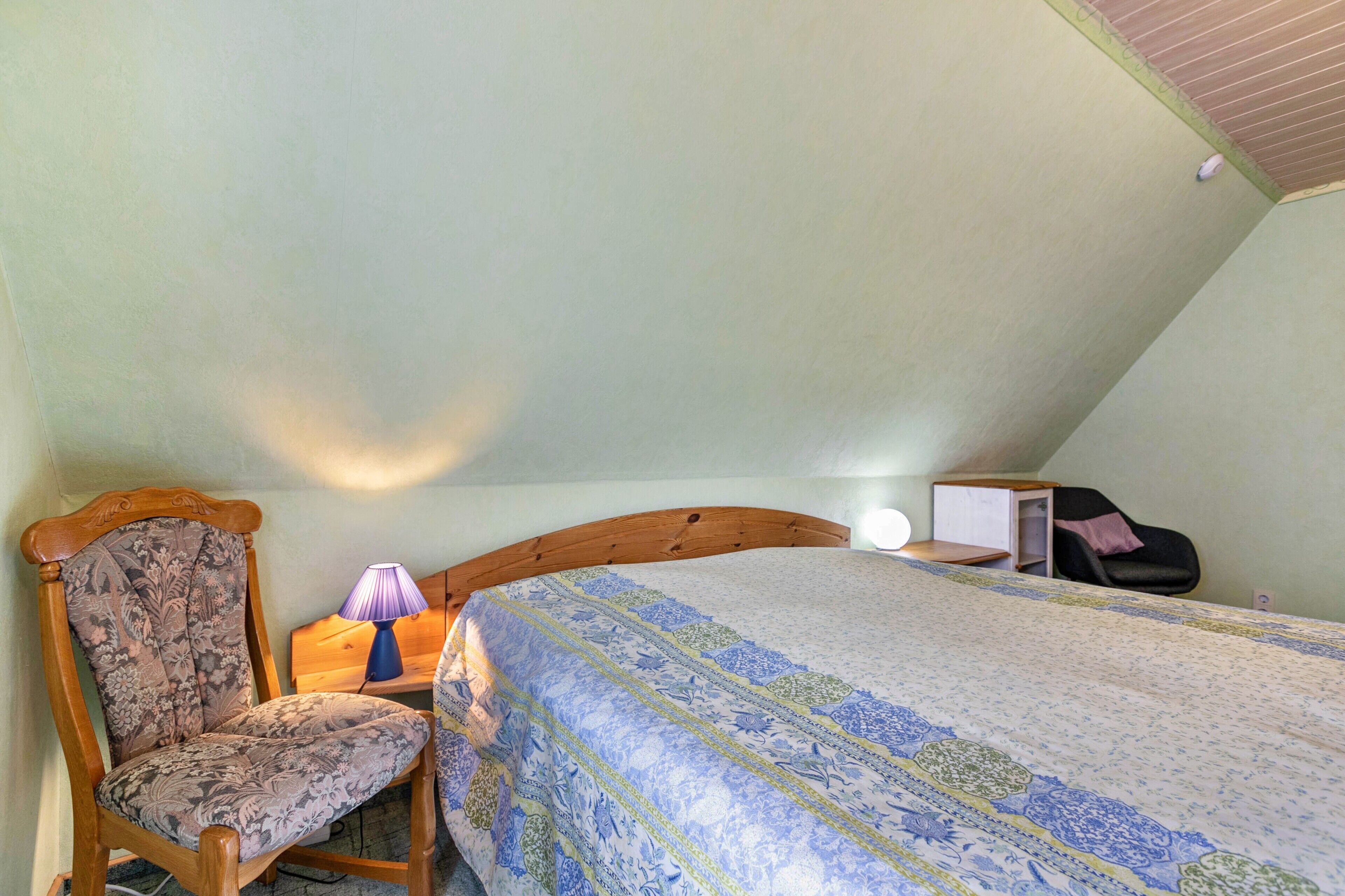 Une chambre à coucher comprenant un lit, une chaise, une table de chevet, une lampe et un bureau.