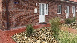 Un edificio de ladrillo con techo de tejas rojas, un cartel que dice 'Fischerweg 9', y una pequeña zona ajardinada con piedrecitas y plantas.