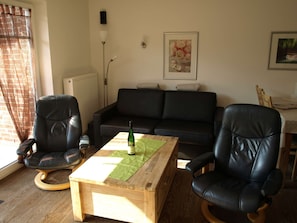 A living room with a black leather sofa, two black leather chairs, a wooden coffee table with a bottle, a radiator, a lamp, and a framed picture on the wall.