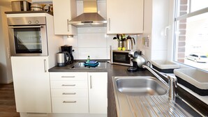 Cocina compacta con horno, microondas, tetera y ventana con vista a un coche.