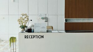 A reception desk with a sign reading "RECEPTION", a telephone, a small plant, and a wall-mounted light fixture. - Amerta Room Patraland Urbano (Bekasi)