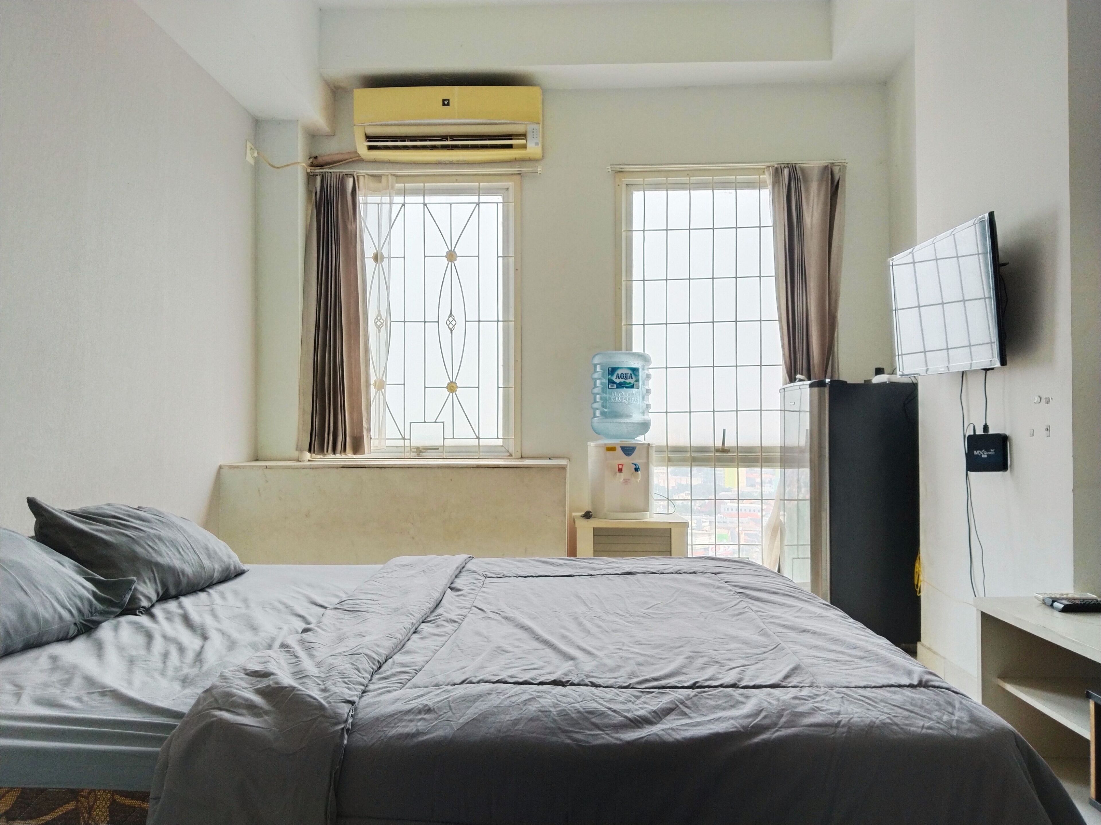 A hotel room with a bed, a water dispenser, a television, and a window with curtains.