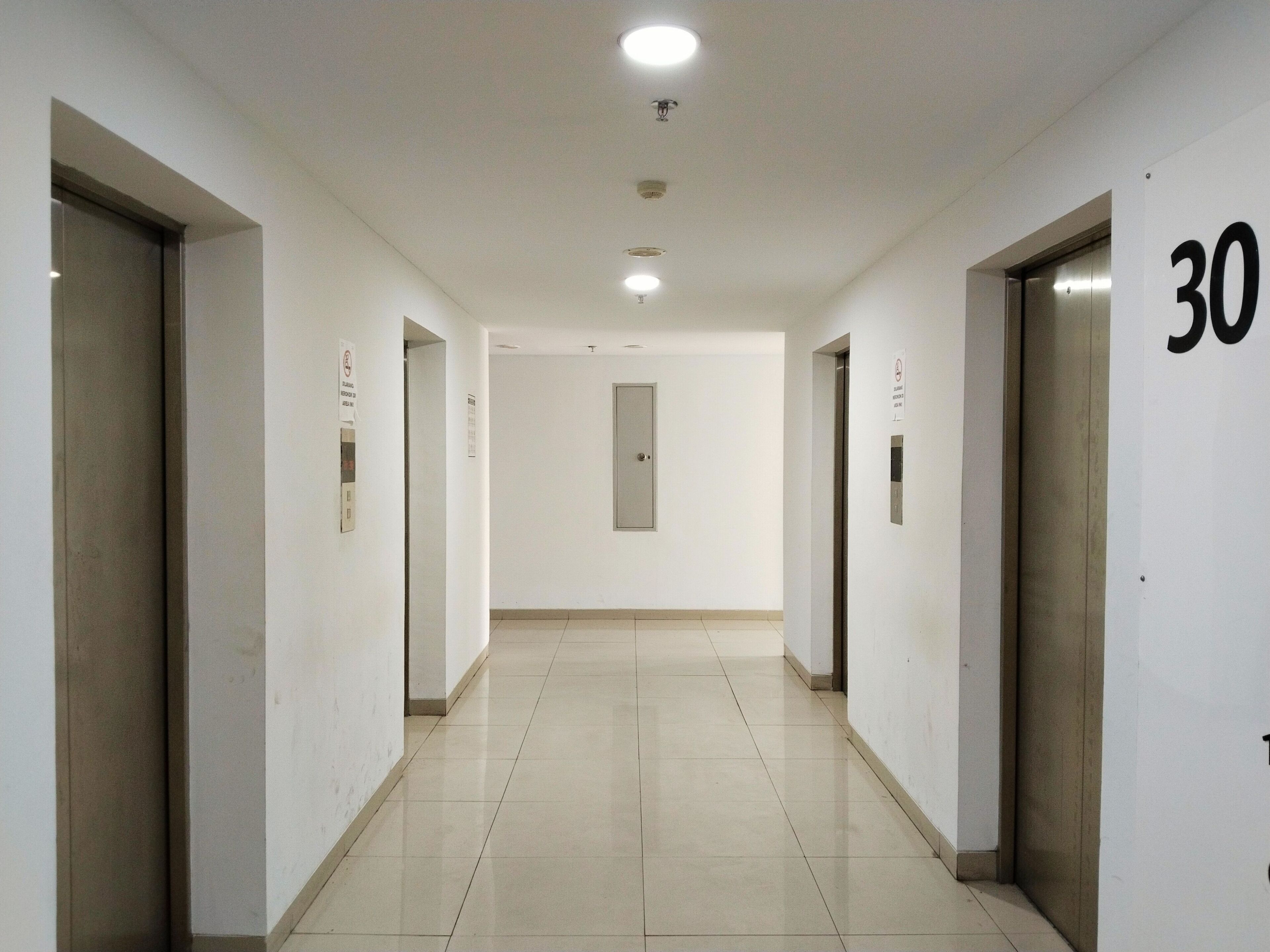 A hallway with a tiled floor, doors on both sides, and a number 30 sign on the right wall.