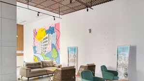 A spacious lobby with a modern design, featuring a large abstract mural, comfortable seating, and informational posters. - Amerta Room Patraland Urbano (Bekasi)