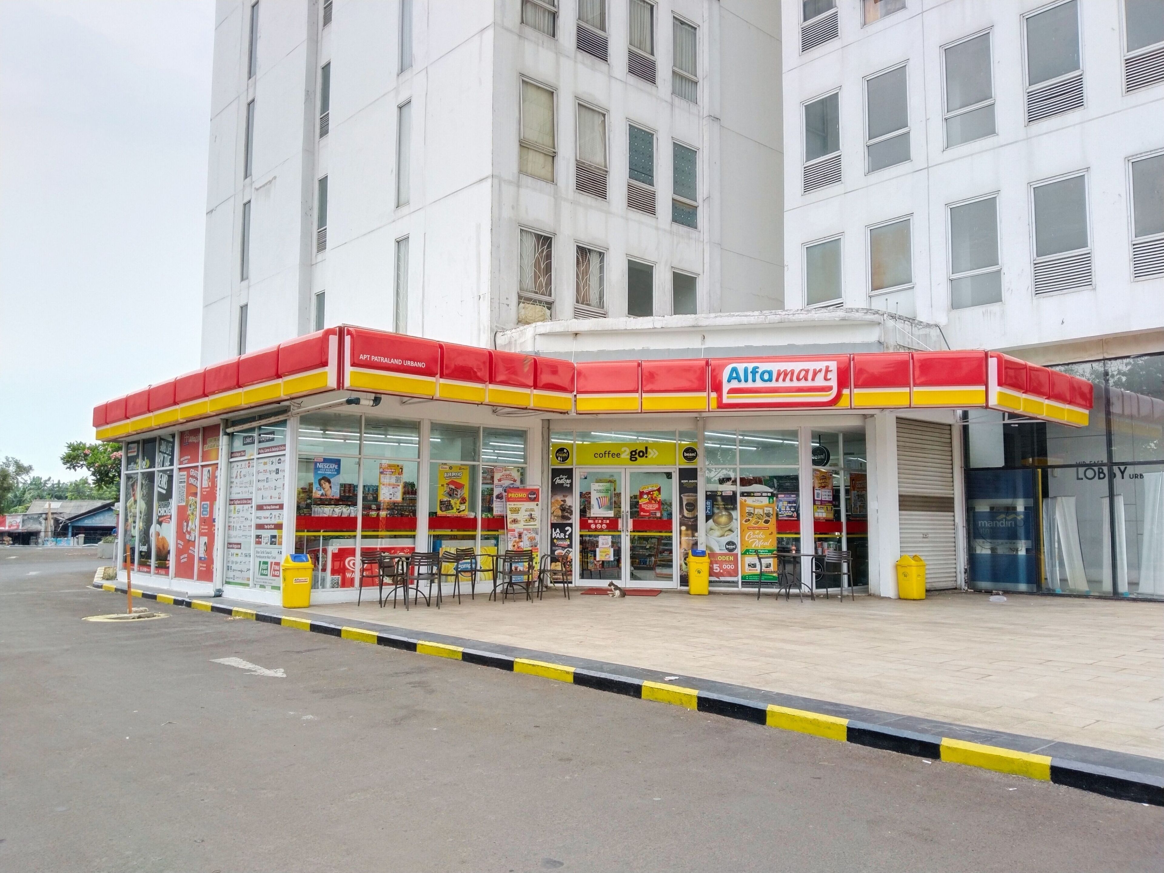 Tankstelle mit rotem und gelbem Vordach, mehreren Zapfsäulen und verschiedenen Werbeanzeigen.
