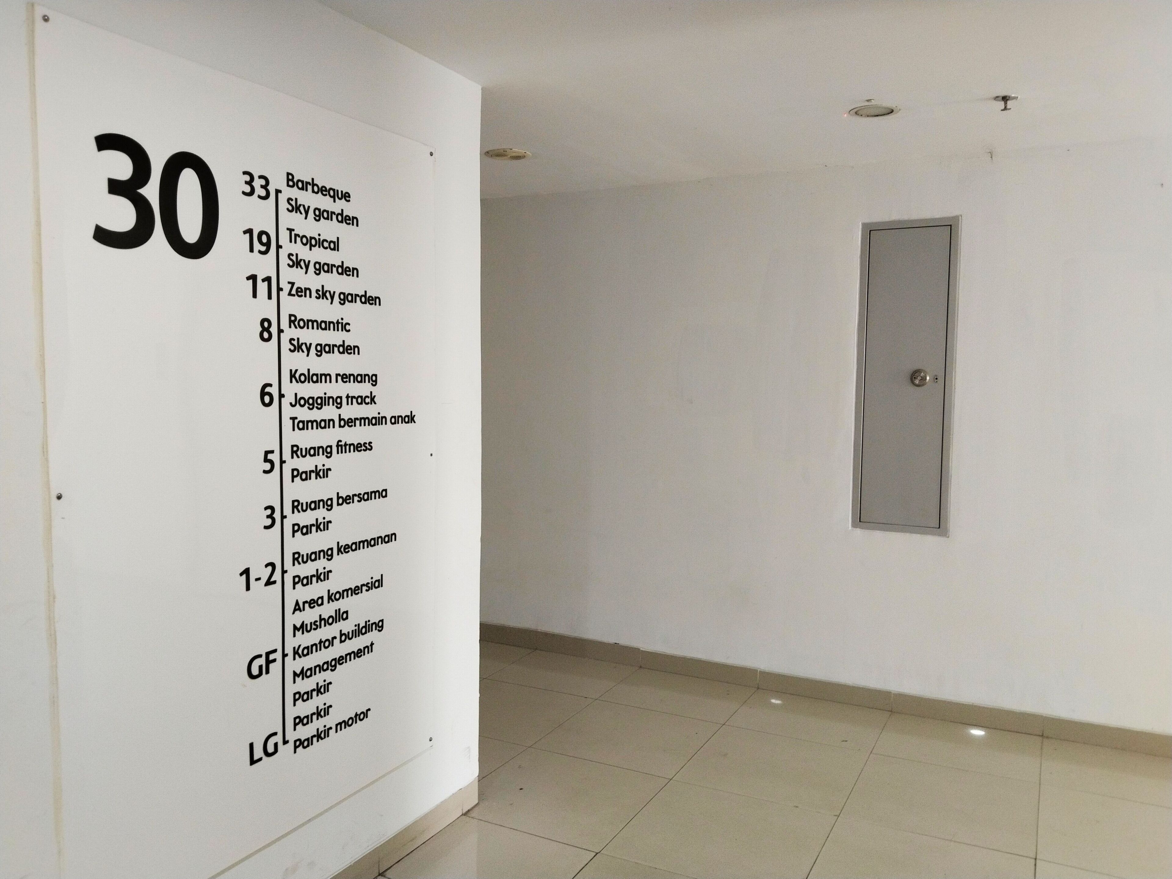 A hallway with a white wall displaying a list of amenities and room numbers.