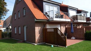 Una casa de dos pisos con techo de tejas rojas, un balcón y un patio trasero cercado.