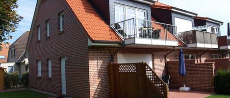 Una casa de dos pisos con techo de tejas rojas, un balcón y un patio trasero cercado.