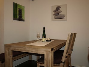 Una mesa de madera para comer con dos copas de vino y una botella, sobre un posavasos blanco.