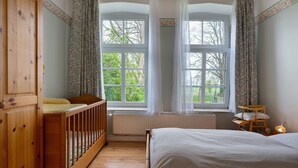 A bedroom with a wooden crib, a bed, a chair, and a window with curtains. - Apartment 'Große Ferienwohnung' with Shared Terrace, Shared Garden and Wi-Fi (Leck)
