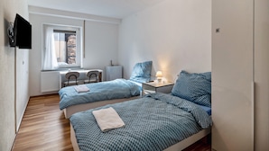 Une chambre avec deux lits, un bureau, une chaise, un radiateur et une fenêtre avec des rideaux.
