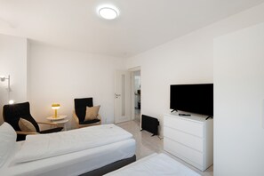 Une chambre d’hôtel avec un lit, deux chaises, une télévision, un bureau et une commode.