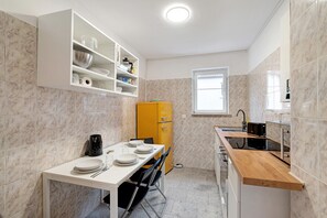 Une cuisine de taille réduite, dotée d’un plan de travail blanc, d’un réfrigérateur jaune et d’une fenêtre laissant entrer la lumière naturelle.