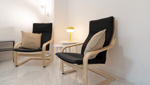 Two modern chairs with black cushions and wooden frames, a small white table with a yellow lamp, and a white wall. - Apartment 'Die Edisonstraße' with Wi-Fi (Pforzheim)
