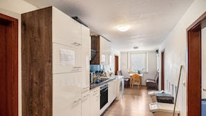 Un couloir étroit avec un coin cuisine sur la gauche, comprenant des meubles blancs, un mur d’accent en bois et un lave-linge.