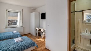 Une chambre avec deux lits, un bureau, une chaise, une télévision et une salle de bain avec un lavabo.