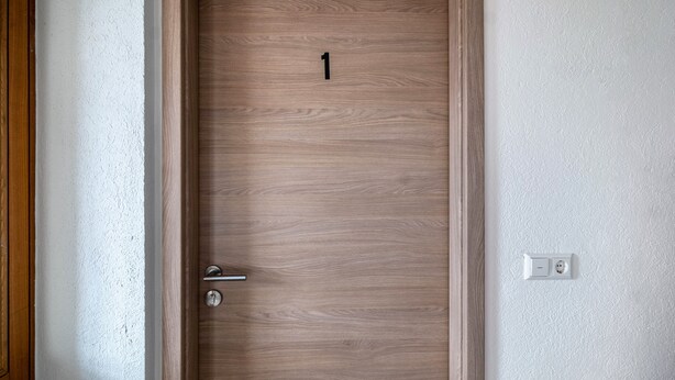 Une porte en bois portant le numéro 1, une poignée de porte et un interrupteur sur le mur.