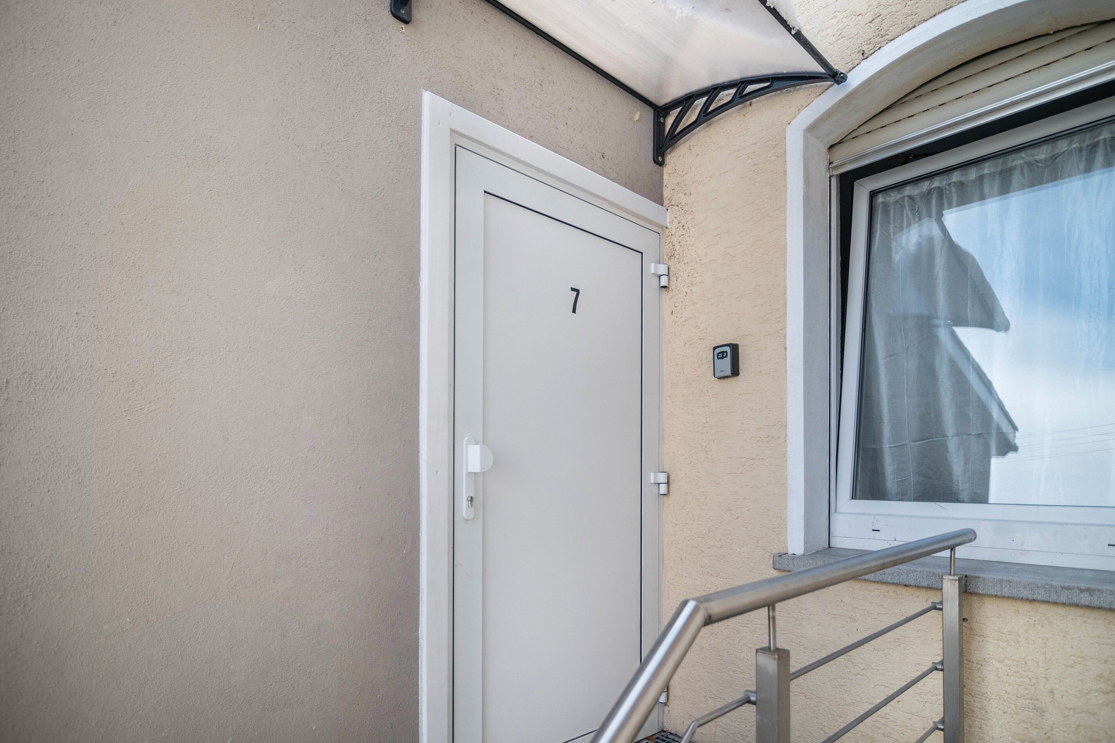 A door with the number 7, a window with a curtain, and a metal handrail.