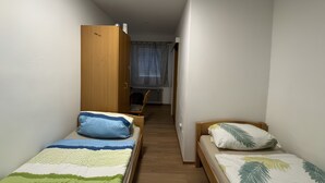 Une petite pièce avec deux lits simples, une armoire en bois, une chaise et un radiateur.