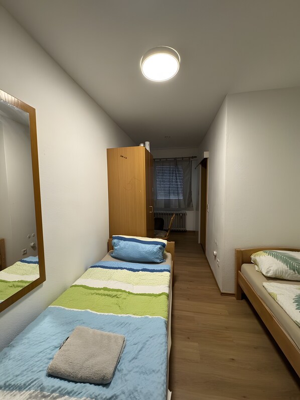 A bedroom with two beds, a wooden wardrobe, a mirror, and a ceiling light. - Room 'Zimmer 8' with Wi-Fi (Berg-Weiler)