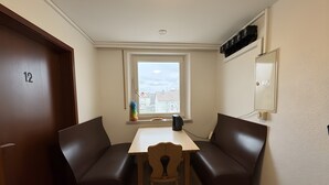 A room with a table and two brown leather benches, a window with a view of buildings, a door with the number 12, and a wall-mounted mirror. - Room 'Zimmer 10' with Wi-Fi (Berg-Weiler)