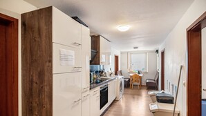 A narrow hallway with a kitchen area on the left, featuring white cabinets, a wooden accent wall, and a washing machine. - Room 'Zimmer 10' with Wi-Fi (Berg-Weiler)