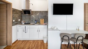 A modern kitchen with a built-in stove, a TV mounted on the wall, and a dining area with chairs. - Room 'Zimmer 4' with Wi-Fi (Berg-Weiler)