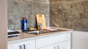 A kitchen with a granite backsplash, a stainless steel sink, a wooden cutting board, a blue bottle, and a pink cloth. - Room 'Zimmer 4' with Wi-Fi (Berg-Weiler)