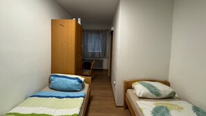 Une petite pièce avec deux lits simples, une armoire en bois, une chaise et un radiateur.
