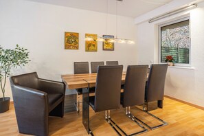 Un espace repas moderne avec une table en bois, six chaises et trois luminaires fixés au mur.