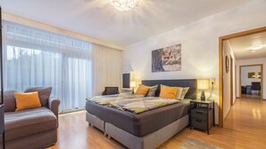 A modern bedroom with a large bed, a sofa, a bedside table, and a window with sheer curtains. - Apartment 'Das Spatzennest' with Sauna, Mountain Views & Private Terrace (Bad Harzburg)