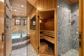 En sauna med træbænke, en stenvæg og et glasomkranset spabad.