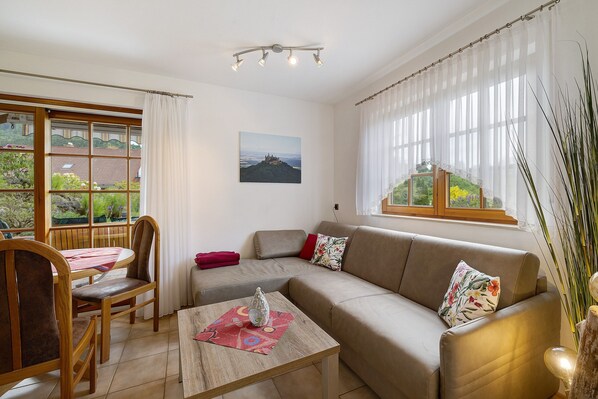 Una sala de estar con un sofá, una mesa de comedor con sillas, una ventana con cortinas y un cuadro en la pared.